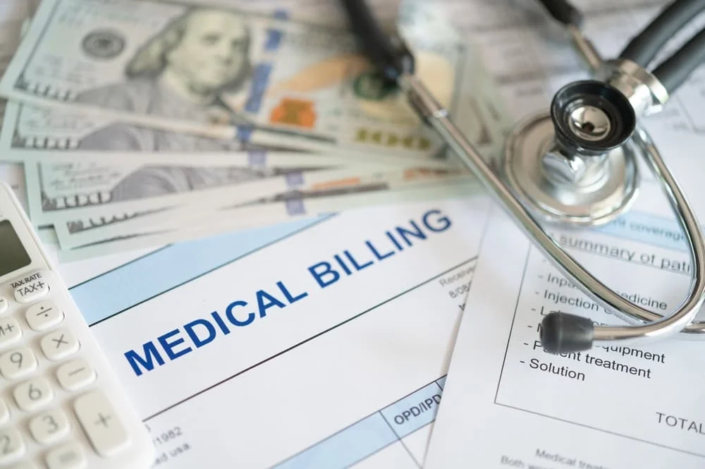 Medical billing document and dollar banknote, calculator, stethoscope.
