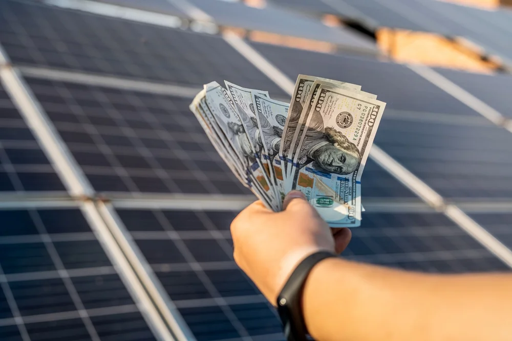 Money in hand of a man and front of solar panel